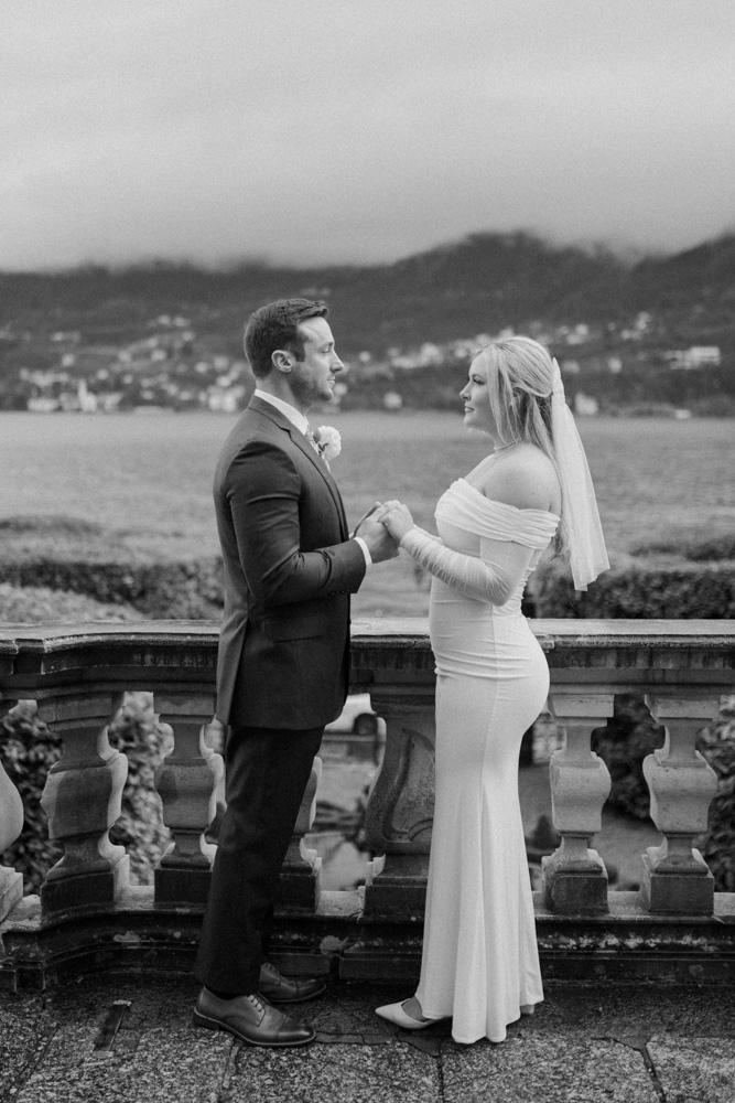 A black and white picture for the couple holding their hands on the balcony over the Como lake