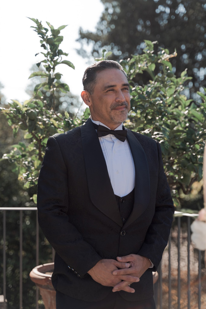 The groom in a black classic Tuxedo facing the bride