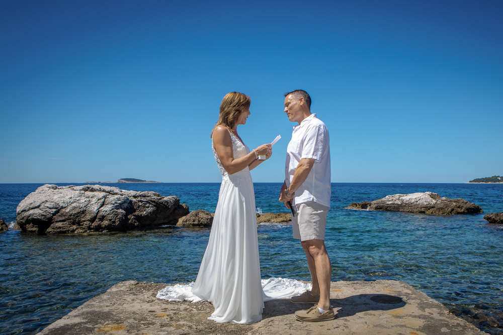 The bride reads her vows to the groom during the ceremony. They stands on a pier close to the sea