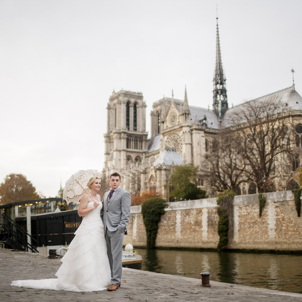 The couple walk on the river bank in front of Notre Dame