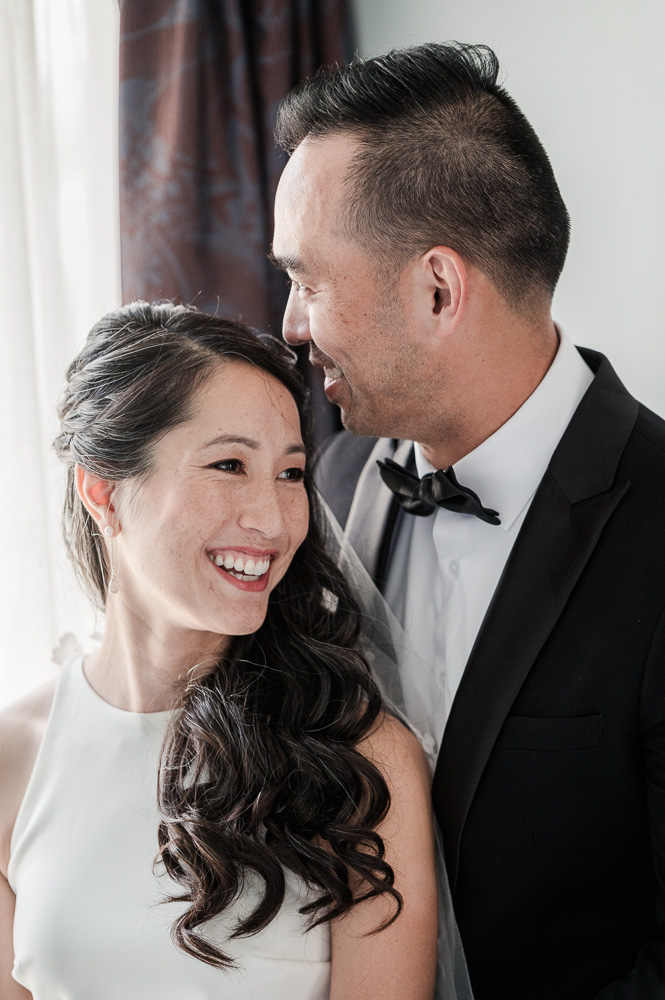 Th esmiling bride with the happy groom in front of th e window for a pretty light