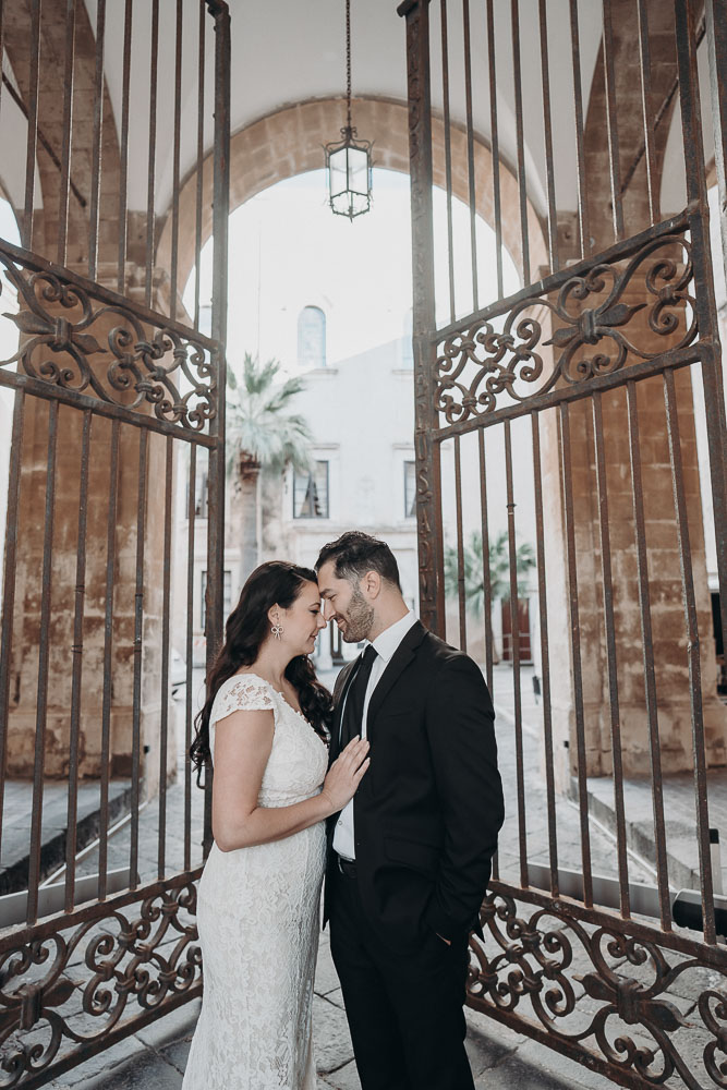 Forehead against forehead, the husband and wife stands in front of a vintage gate in steel